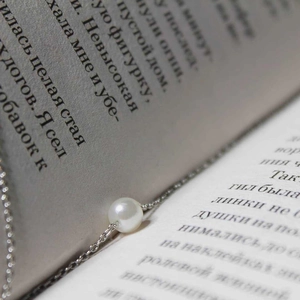 Macro shot of an elegant white pearl pendant on a fine silver chain over an open book