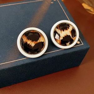 Close-up of leopard print round earrings with faceted design on a navy blue jewelry box