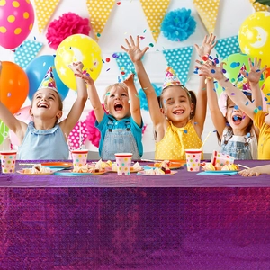 Vibrant party scene showing four kids behind a long table with a purple sequin tablecloth