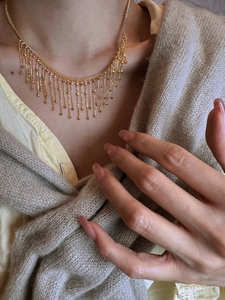 Close-up of elegant gold tassel necklace with fine bead chains on a cozy knit cardigan