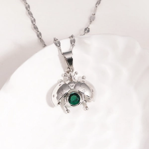 Detail of silver titanium chain with enamel ladybug pendant and green gemstone inlay