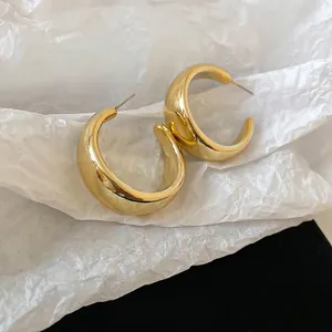 Minimalist wide C-shape gold earrings with glossy metallic finish on a textured background