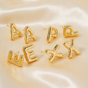 Detailed macro view of 3D gold balloon letter stud earrings on silk background