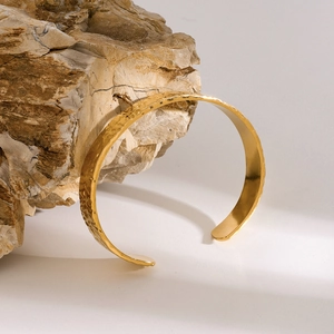 Detalle del brazalete de acero inoxidable dorado con patrón de ondas sobre piedra