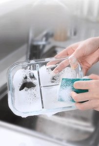 Close-up of dual-sided kitchen sponge cleaning a glass bowl with rich soapy foam