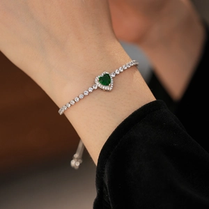 Detail shot of heart-shaped green zircon bracelet worn by a model on a silver chain