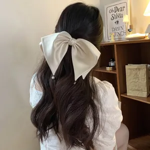 Elegant cream white silk satin bow hair clip with pearl drops on wavy hair for women