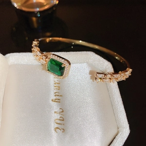 Macro shot of an open gold bangle featuring a large emerald-cut stone and pavé diamonds