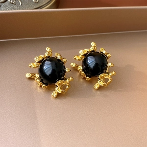 Close-up of vintage gold lava texture earrings with a large black bead on a tray