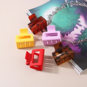 Five matte 5cm square hair claws in assorted macaron colors on a fashion magazine