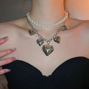 Detail of double-layer necklace with white pearls and five silver heart pendants on a model
