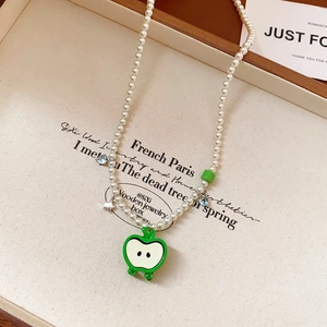Détail d'un collier de perles avec pendentif pomme verte, étoiles et cœurs sur plateau