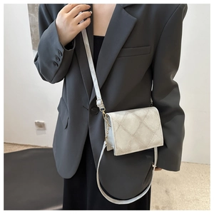 Detail of quilted beige crossbody bag with gold buckle on a grey suit model
