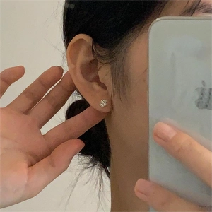 Close-up of minimalist sterling silver flower stud earring shown on the ear in a mirror selfie