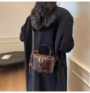 Detail of a dark brown glossy leather box bag with gold hardware worn by a model
