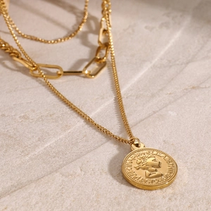 Detail of triple-layer gold necklace featuring an Elizabeth II coin pendant on stone background