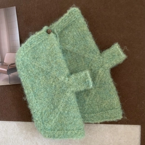 Close-up of light green hand-knitted gloves with textured plush yarn and a dark button