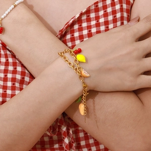 Close-up of a fruit-themed charm bracelet featuring cherry and lemon on a gold chain