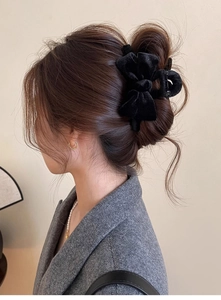 Detail of a large black velvet bow hair claw clip worn on a model's hair with a soft background