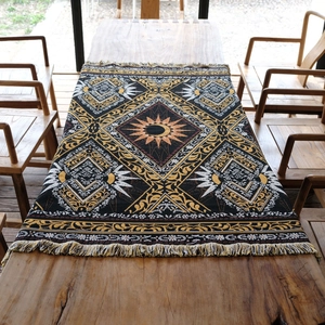 Bohemian woven camping blanket with sun mandala pattern and tassels on wooden table