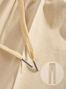 Detailansicht der beigen Twill-Stoffstruktur und Kordelzug mit Metallenden an der Hose