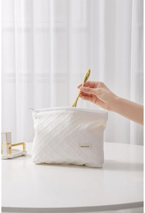 Dettaglio della borsa da toilette trapuntata bianca con etichetta H&R e motivo a griglia