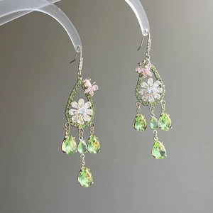 Macro detail of gold-plated drop earrings with green zircon butterfly and flower motifs