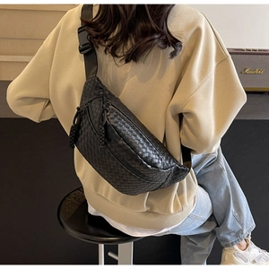 Detail of woven black leather chest bag with adjustable strap shown on model outdoors
