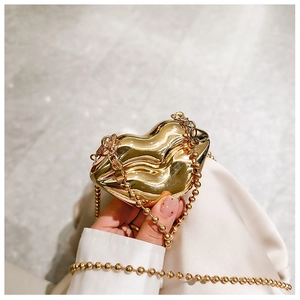 Close-up of a gold lip-shaped metal evening clutch with beaded chain strap held by hand