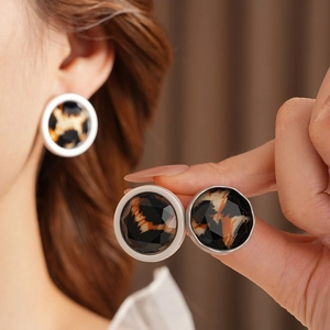 Close-up of model wearing round leopard print earrings with faceted glass and silver rim