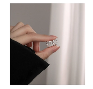Close-up of heart-shaped hollow earrings in polished silver finish being held for size