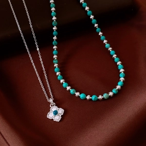 Close-up of turquoise beaded necklace and silver flower pendant on brown silk fabric