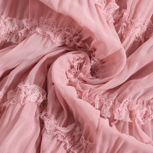 Close-up of pink textured fabric with delicate lace trim on backless pleated dress