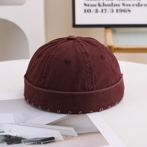 Detail of burgundy distressed cotton brimless docker cap with frayed edges on a table