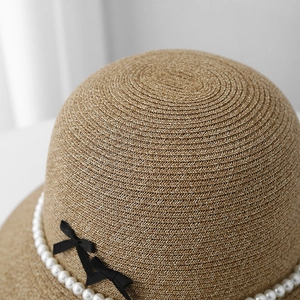 Close-up of woven straw sun hat featuring elegant pearl chain and black ribbon bows