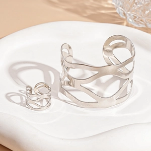 Gros plan d'un ensemble bracelet et bague argentés ajourés sur plateau minimaliste