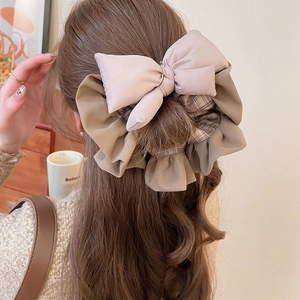 Detail view of a layered pink and plaid bow hair tie worn on a high ponytail