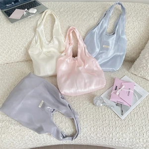 Detailed close-up of four satin tote bags in cream, pink, blue, and grey on a sofa