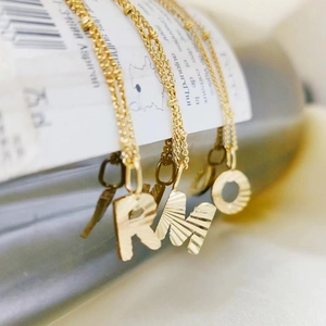 Close-up of 18k gold plated stainless steel necklaces with R, M, O and key pendants