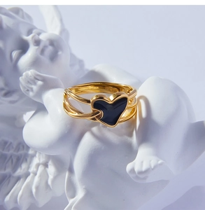 Vue macro d'une bague dorée multicouche avec cœur en émail noir contre sculpture blanche