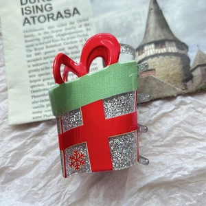 Detail view of silver glitter Christmas gift box hair claw clip with red bow and snowflakes