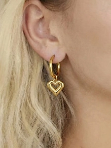 Close-up of gold hoop earrings with hollow heart pendants worn by a model in soft light