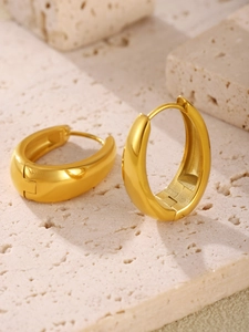Detailed view of chunky gold hoop earrings on a matte stone surface in natural lighting