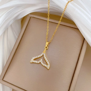 Detailed close-up of a hollow zircon fish tail pendant on a gold chain over white silk