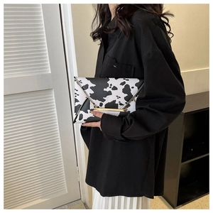 Detail of a cow print envelope clutch with golden metal trim and sleek PU leather texture