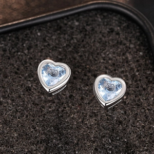 Close-up of heart-shaped silver earrings with light blue faceted zircon on black foam