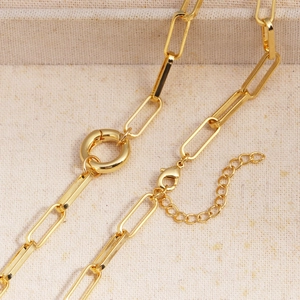 Macro shot of gold plated paperclip chain necklace with a ring pendant on beige linen