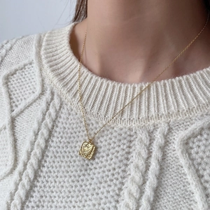 Close-up of gold leaf-textured rectangular pendant necklace on a white knit sweater