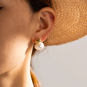 Detail of elegant gold earring featuring a round white pearl on a sunny model photo