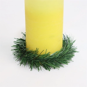 Macro shot of green PVC pine needle candle ring surrounding a yellow pillar candle